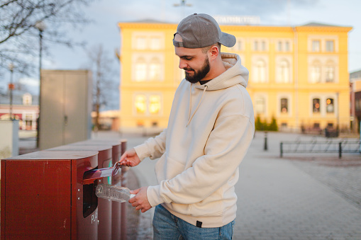 Young man throwing away his plastic bottle in a recyclable container.