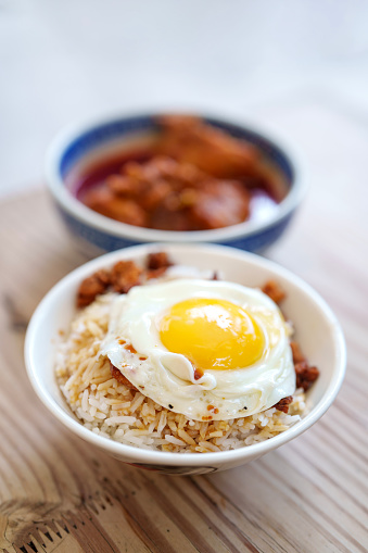 Close up a bowl of crispy pork lard mixed rice with fried egg and a bowl of curry chicken