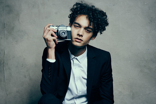 curly-haired man in a jacket and shirt holding a camera in his hand model vogue style. High quality photo
