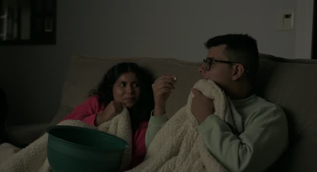 Young people get scared while watching a horror movie on TV at home at night