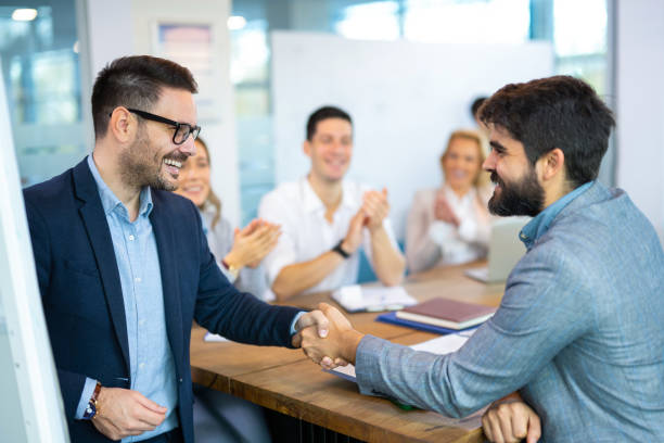 istock Business men shaking hands while co-workers in the background applauding and celebrating successful agreement. 2083437135