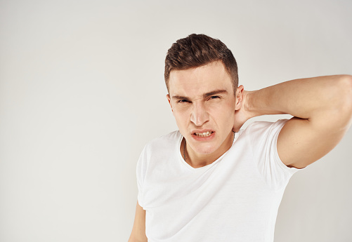 A guy in a white T-shirt emotions irritability light background inadequate state. High quality photo