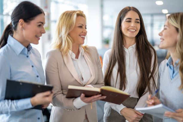 istock Multi-aged business women with paper documents standing in office interacting with each other, brainstorming creating sales strategy for their company. 2083446700