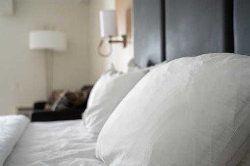 Side view and close-up on big white pillow on a bed with white sheets with brown head bed