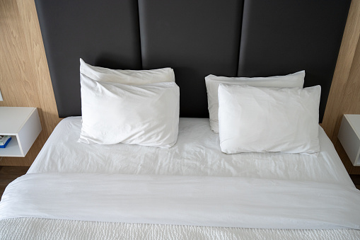 Bed with white sheets and big white pillow with brown head bed