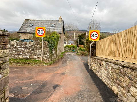 Humorous street scene with conflicting 20mph and 30mph speed limit signs on opposite sides of the road, causing confusion. Wales, UK.