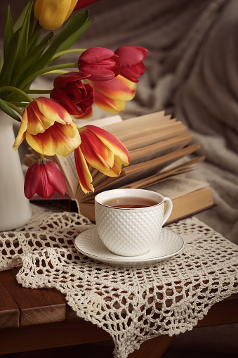Photo of a cup of tea near a bouquet of tulips.