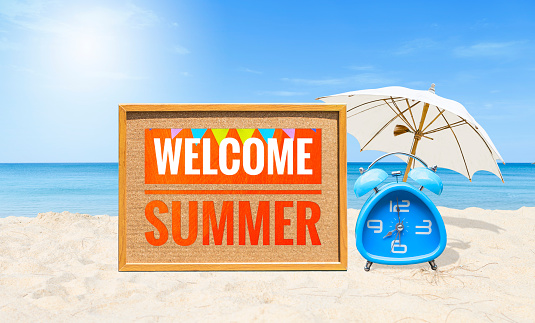 Welcome summer sign with blue alarm clock and white umbrella on tropical beach, outdoor day light