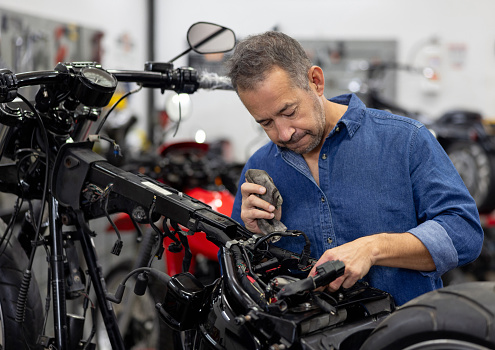 Latin American mechanic repairing a motorcycle at a garage - vehicle breakdown concepts