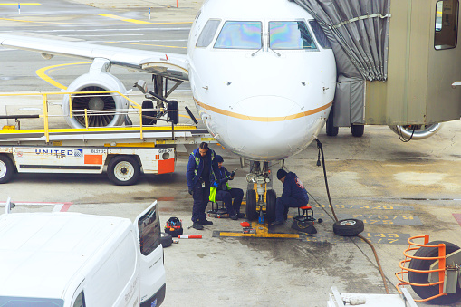 30 October 2023 EWR Newark NJ US United Airlines aircraft Aircraft maintenance mechanics at work in sitting on his haunches under plane