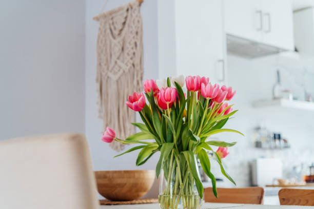 istock Stylish and modern boho, scandi interior of open space white kitchen with pink tulip flowers in vase on the wooden kitchen counter table, macrame on the wall. Cozy Design home decor. Selective focus 2083559729