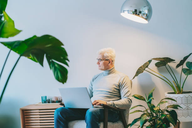 istock Middle-aged man looking aside while working on laptop while sitting in armchair at home. Confident, experienced senior male professional. Small business entrepreneur manage business at home. 2083559738