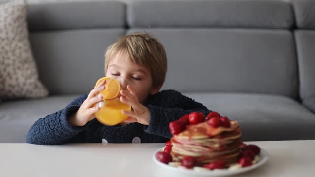 Sweet toddler child, boy, eating american pancakes with strawberries and bananas, topped with syrup