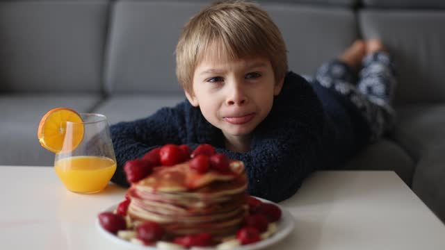 Sweet toddler child, boy, eating american pancakes with strawberries and bananas, topped with syrup