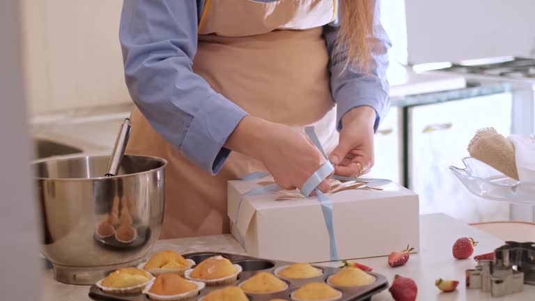 A woman pastry chef packaging cupcakes into a box. Home baking, small business, eco-friendly production, gluten-free, sugar-free, promoting healthy eating habits.