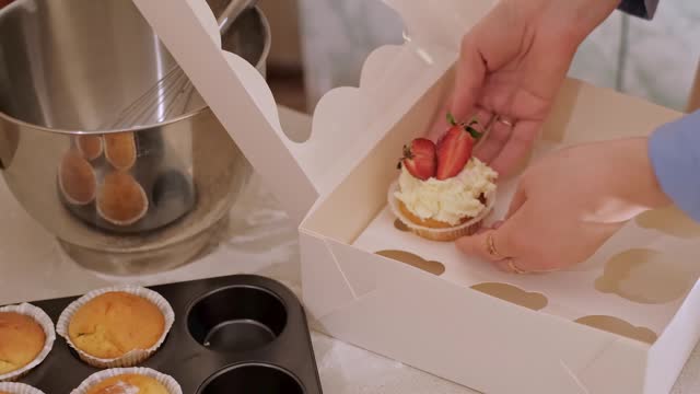 A woman pastry chef packaging cupcakes into a box. Home baking, small business, eco-friendly production, gluten-free, sugar-free, promoting healthy eating habits.