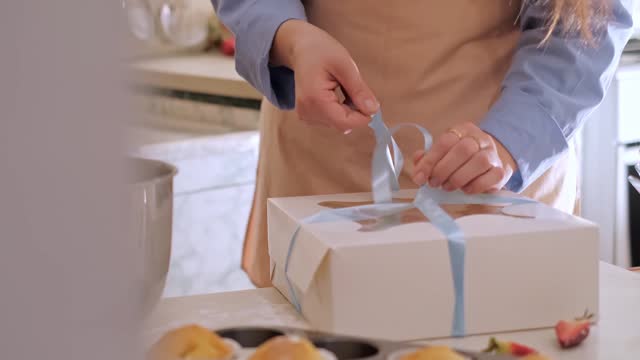 A woman pastry chef packaging cupcakes into a box. Home baking, small business, eco-friendly production, gluten-free, sugar-free, promoting healthy eating habits.