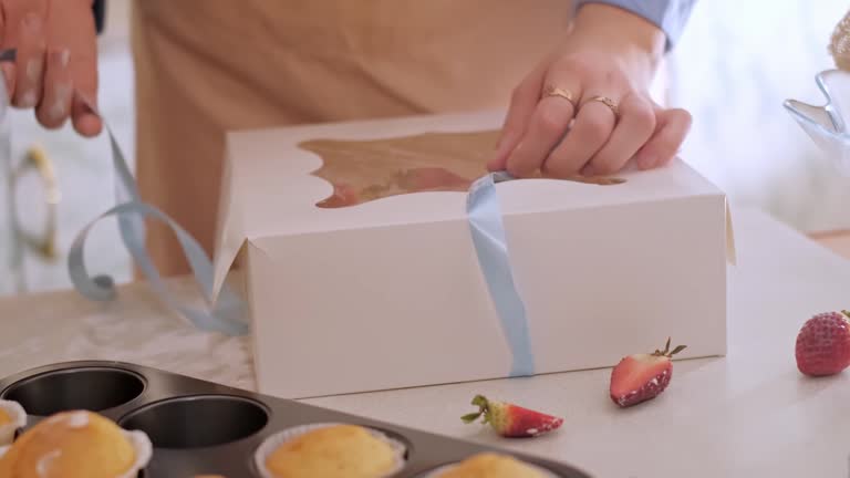 A woman pastry chef packaging cupcakes into a box. Home baking, small business, eco-friendly production, gluten-free, sugar-free, promoting healthy eating habits.