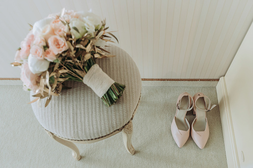wedding bouquet of roses and various flowers on a chair in the wedding room. Pink high-heeled women's shoes on the floor