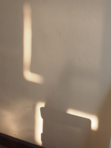 A striking L-shaped shadow shines on the cream-colored wall.
