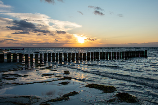 Beautiful orange sunset over the sea, with wooden breakwater in the water