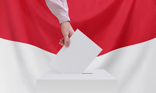 Elections, Indonesia. Election concept. A hand throws a ballot into the ballot box. Indonesia flag on background.