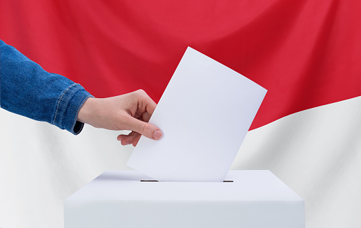 Election concept. A hand throws a ballot into the ballot box. Indonesia flag on background.