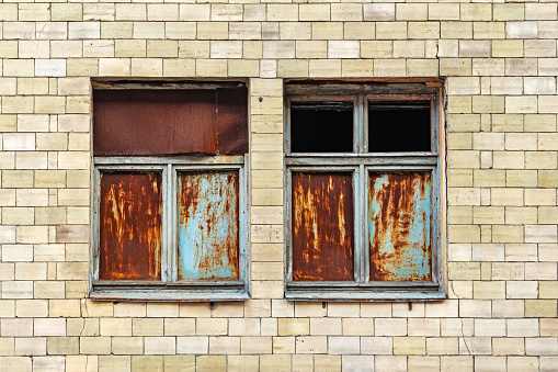 Two windows in the facade of an old abandoned building. Rusty metal sheets in a wooden frame window