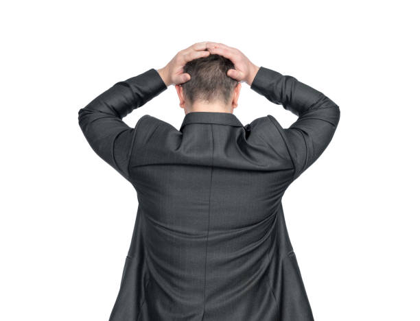 istock A depressed man in a dark suit stands holding his head with both hands, rear view. Isolated white background. File contains a path to isolation. 2083603884