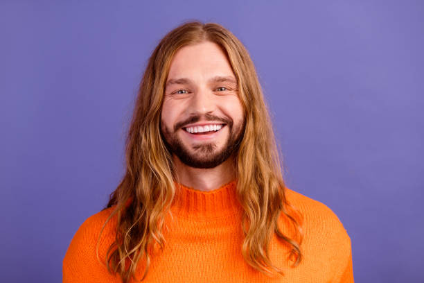 portrait d’un jeune hippie portant un pull orange, de longs cheveux blonds avec une moustache, une dent, souriant, isolé sur fond de couleur violette - beautiful hippie blond hair hair care photos et images de collection