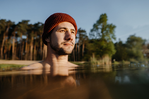 Portrait of morning swim and cold treatment. Young man soaks in the winter lake at morning. Male person taking care of his heath.