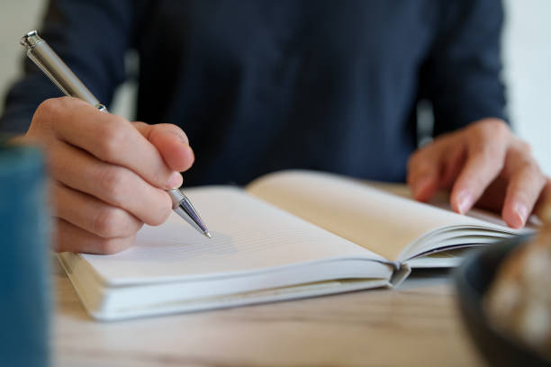 istock Close-up of an Asian woman at a table writing on a notepad while enjoying breakfast with coffee and sourdough bread in the morning. 2083610221