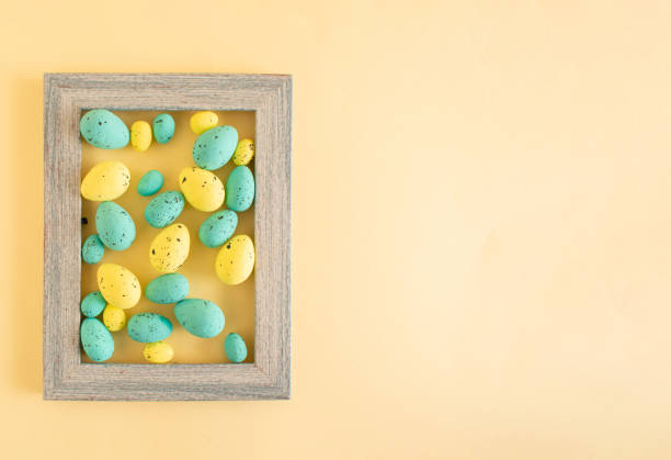 Green and yellow Easter eggs in a picture frame on a pastel yellow background with copy space. Happy Easter concept.