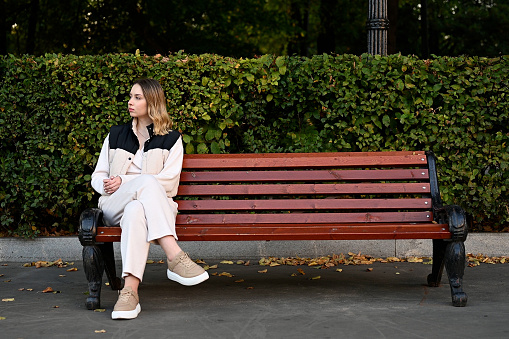 Young lonely woman sitting on a park bench and waiting for someone