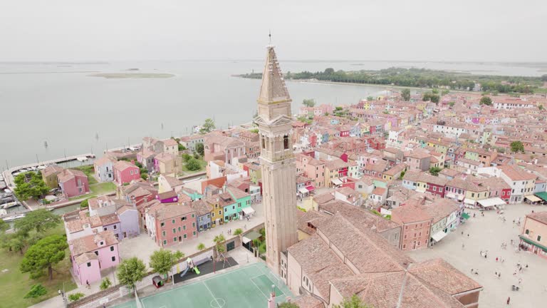 Campanile Storto And Church of Saint Martin Bishop Surrounded By Colorful Houses In Burano, Italy. aerial orbiting shot