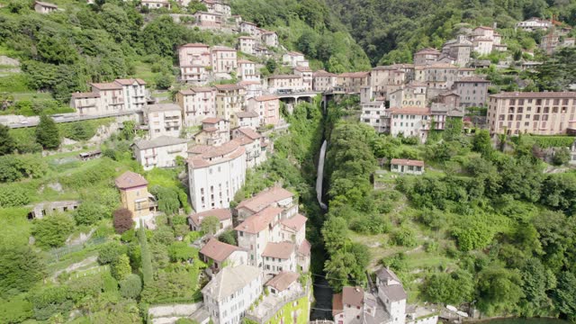 Steep Waterfall Cascading Through Built Structures In Nesso, Como, Italy. aerial static shot