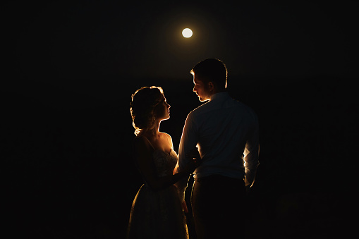 Moonlight highlights the silhouettes of the bride and groom in the mountains.