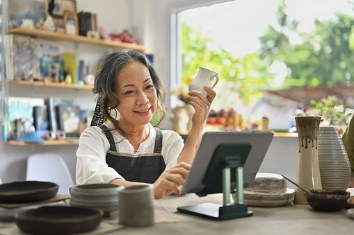 Senior craftswoman with tablet computer in earthenware studio.