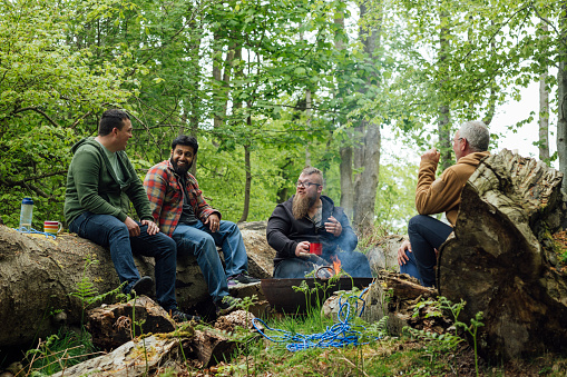 Group of men sitting around a fire pit in a woodland area in Northumberland, North East England. They are enjoying hot drinks while talking.

Videos available for this scenario.