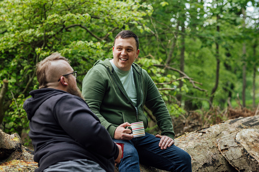 Group of men sitting in a woodland area in Northumberland, North East England. They are enjoying hot drinks while talking.\n\nVideos available for this scenario.