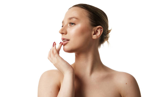 Young beautiful woman with bare shoulders gently touching her lips against white studio background. Profile view.
