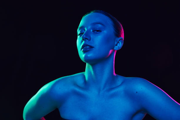 istock Elegant young lady with bare shoulders posing looking at camera in neon light against black studio background. Skin care. 2083696311