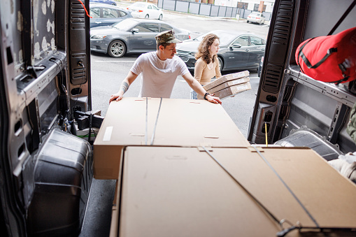 A young couple of Navy soldier and his Caucasian girlfriend examines the contents of the cargo during relocation, taking a box out of the van. Looking from the van