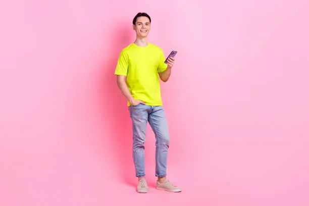 Full length photo of positive funky man dressed yellow t-shirt chatting instagram twitter telegram facebook isolated pink color background.