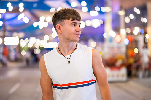 Portrait of handsome caucasian young guy wearing sleeveless t-shirt posing on the city street at night