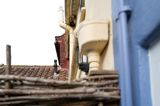 Shallow focus of a newly installed central heating flue pipe seen rising from a distant terraced holiday cottage in the UK. An ornate nature branch fence can be seen separating the two properties.