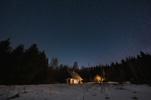 Landscape astrophotography in winter in Estonia. A small wooden house in the forest glows in the dark. Kollassaare. High quality photo