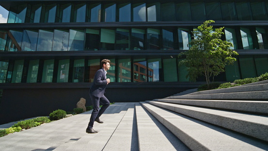 Confident man running stairs up urban street rushing to office work. Rich corporate boss hurrying on business meeting sunny morning. Successful ceo walking staircase modern downtown in elegant suit.