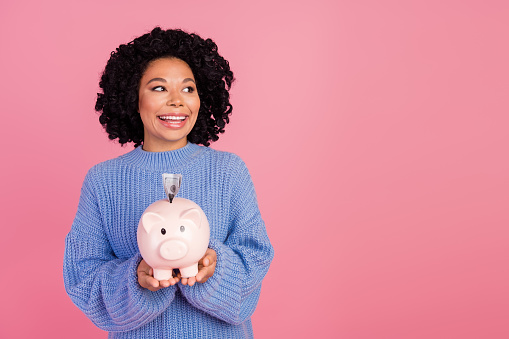 Photo portrait of lovely young lady hold piggy look empty space dressed stylish blue knitted garment isolated on pink color background.