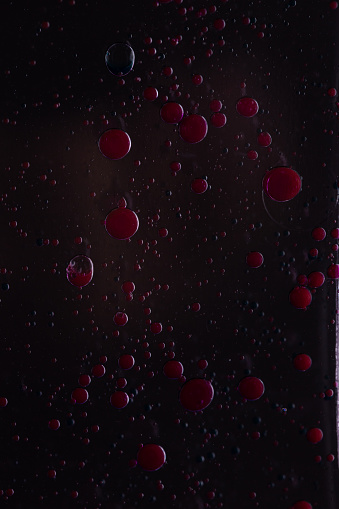 Colored oil bubbles black background red floating in water